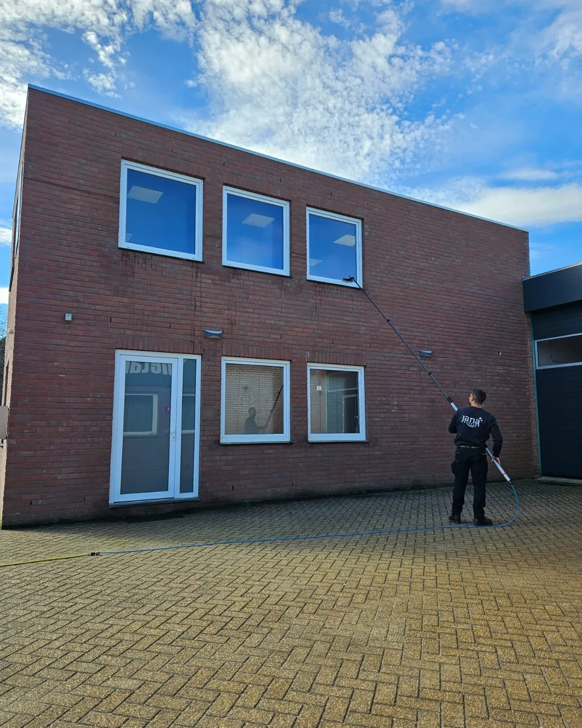 Een van ons team wast de ramen van een bakstenen bedrijfspand, op een geklinkerd plein